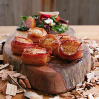 Scallops wrapped in bacon and grilled with maple syrup on wood slab and wood chips with green salad