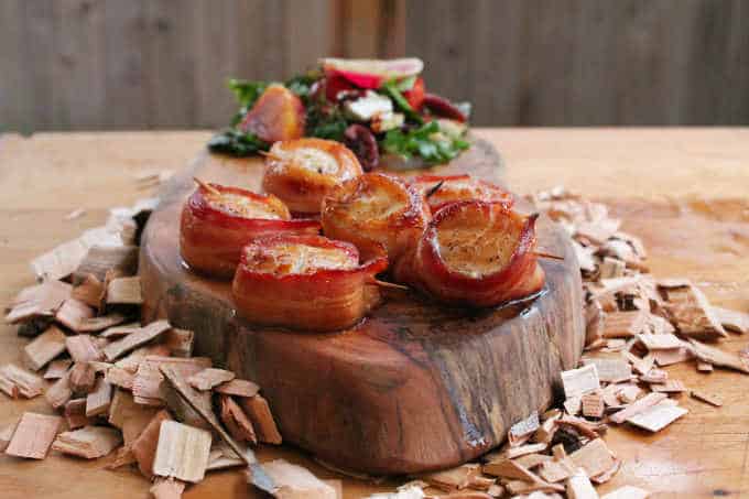 Scallops wrapped in bacon and grilled with maple syrup on wood slab and wood chips with green salad