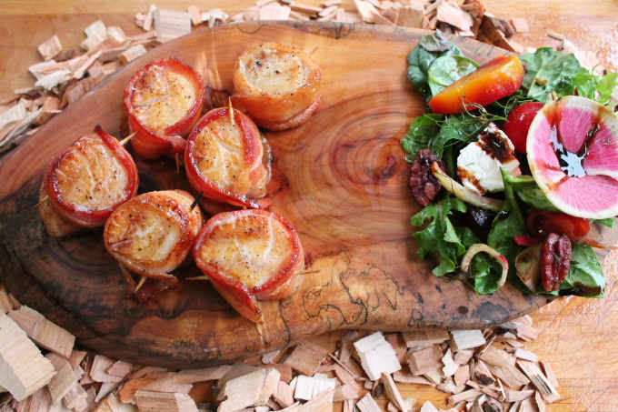 Scallops wrapped in bacon and grilled with maple syrup on wood slab and wood chips with green salad
