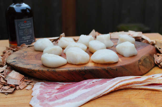 raw scallops sitting on wood slab and cherry wood chips with alder wood smoked maple syrup and bacon slices