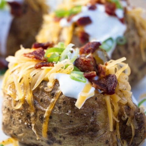 4 air fryer baked potatoes topped with sour cream, cheese, bacon and onions