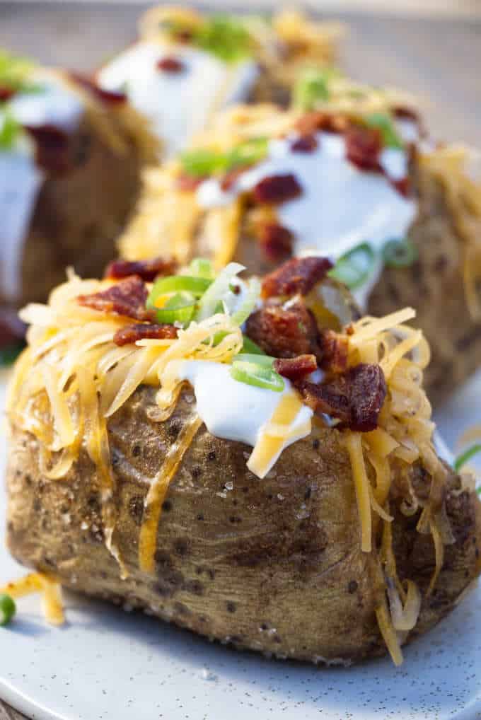 4 air fryer baked potatoes topped with sour cream, cheese, bacon and onions