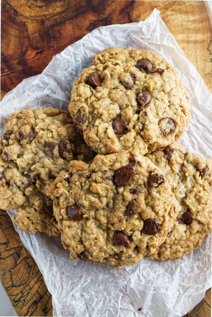 A pile of chocolate chip oatmeal cookies loaded with chocolate chips, resting on parchment paper.