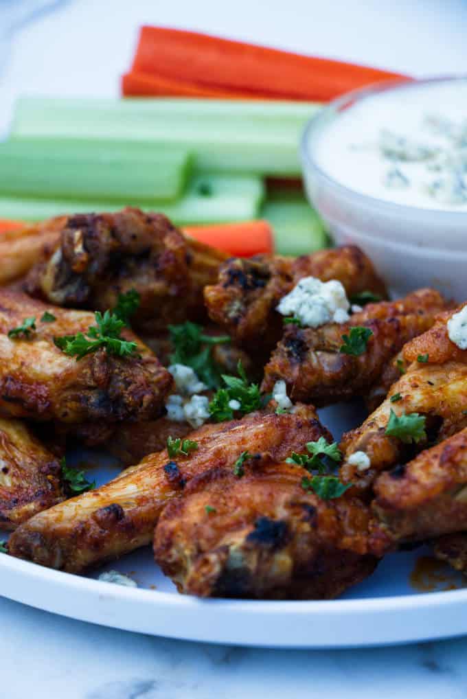 chicken wings with buffalo sauce sitting on a white plate with blue cheese and celery and carrots in the background