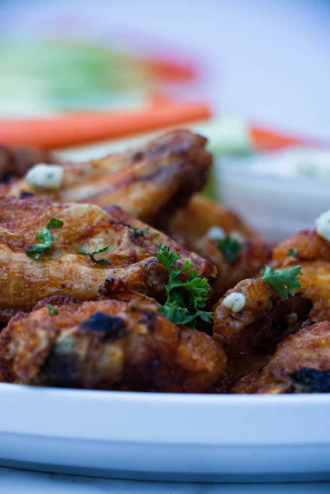 chicken wings with buffalo sauce sitting on a white plate with blue cheese and celery and carrots in the background