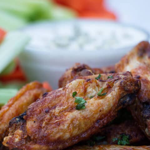 chicken wings with buffalo sauce sitting on a white plate with blue cheese and celery and carrots in the background