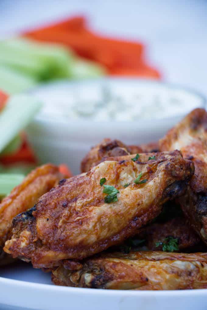 chicken wings with buffalo sauce sitting on a white plate with blue cheese and celery and carrots in the background