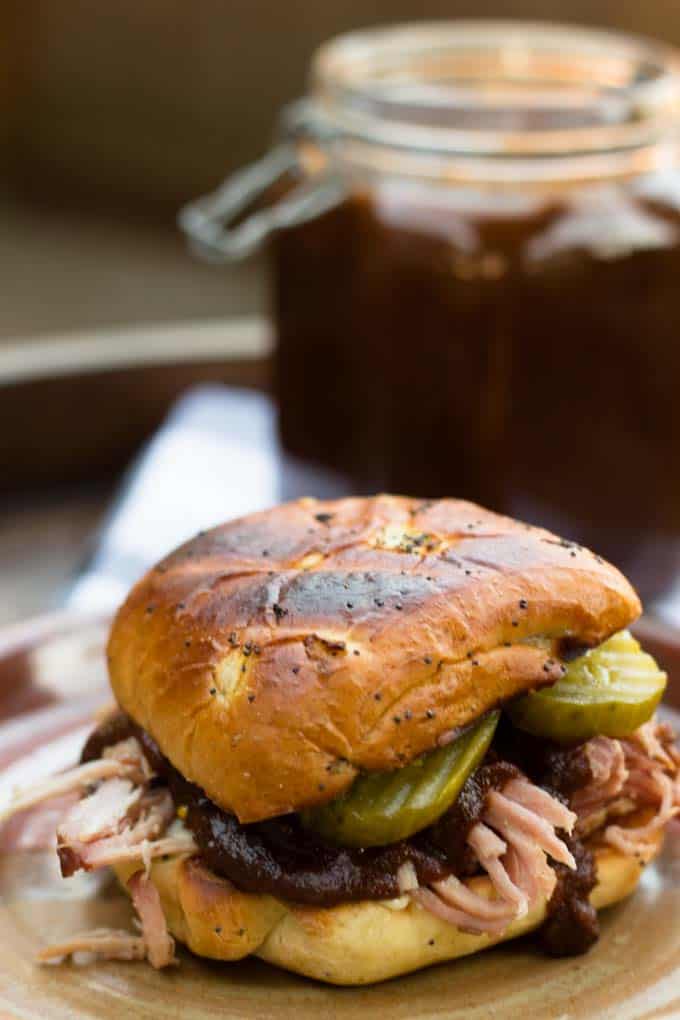 pulled pork with pumpkin spice bbq sauce between buns with pickles and jar of bbq sauce in background