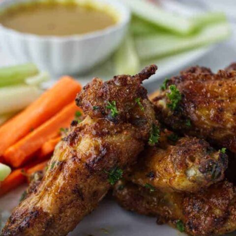 crispy air fried chicken wings sitting on a white plate with sliced carrots and celery with parsley sprinkled on top and dish of honey mustard in background