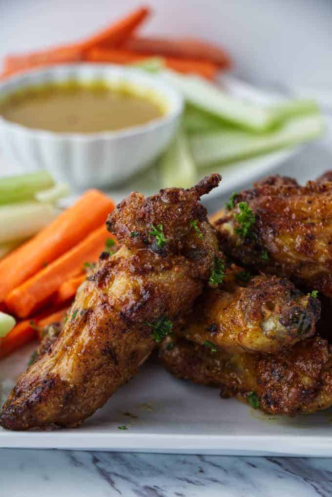 crispy air fried chicken wings sitting on a white plate with sliced carrots and celery with parsley sprinkled on top and dish of honey mustard in background