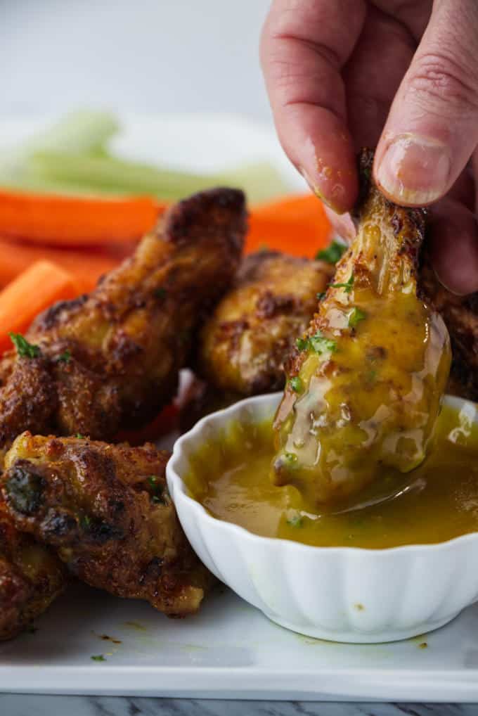 crispy air fried chicken wings sitting on a white plate with sliced carrots and celery with parsley sprinkled on top and one wing being dipped in a dish of honey mustard sauce