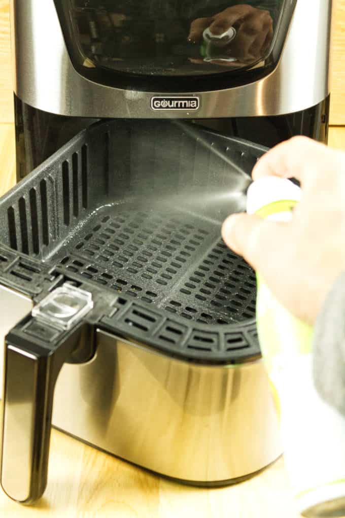 spraying aerosol avocado oil into stainless and black air fryer on wooden table