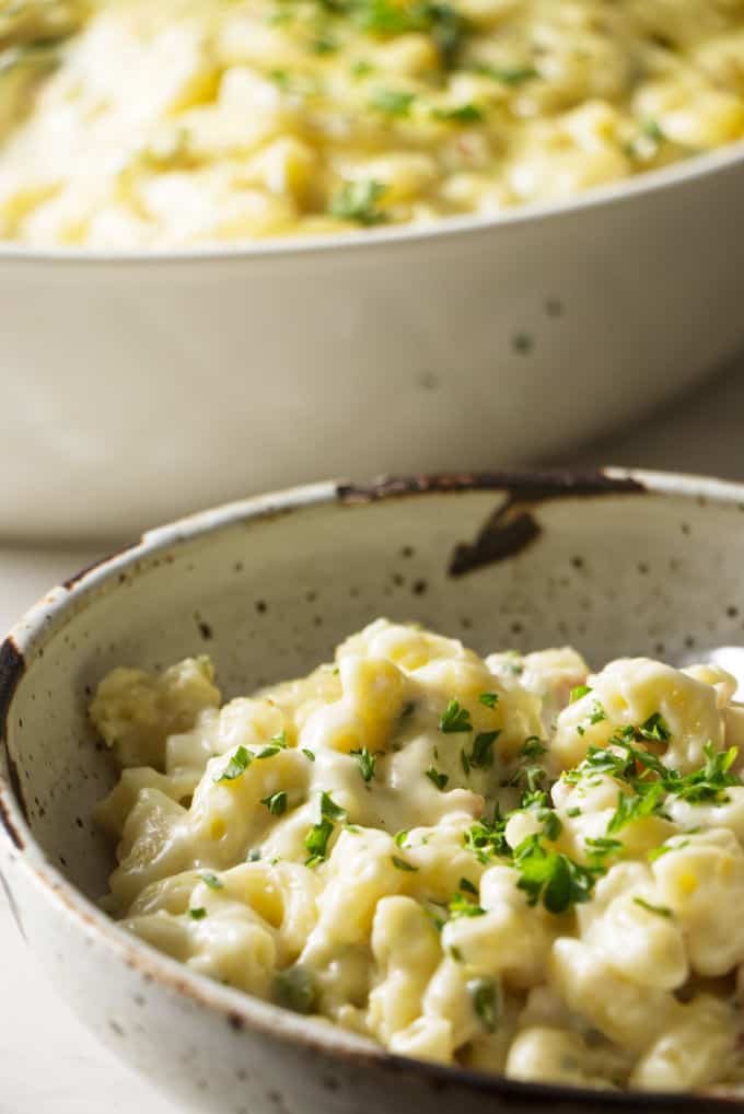 macaroni and cheese in a stone bowl with a spoon and topped with a green garnish. White baking dish in background filled with mac and cheese