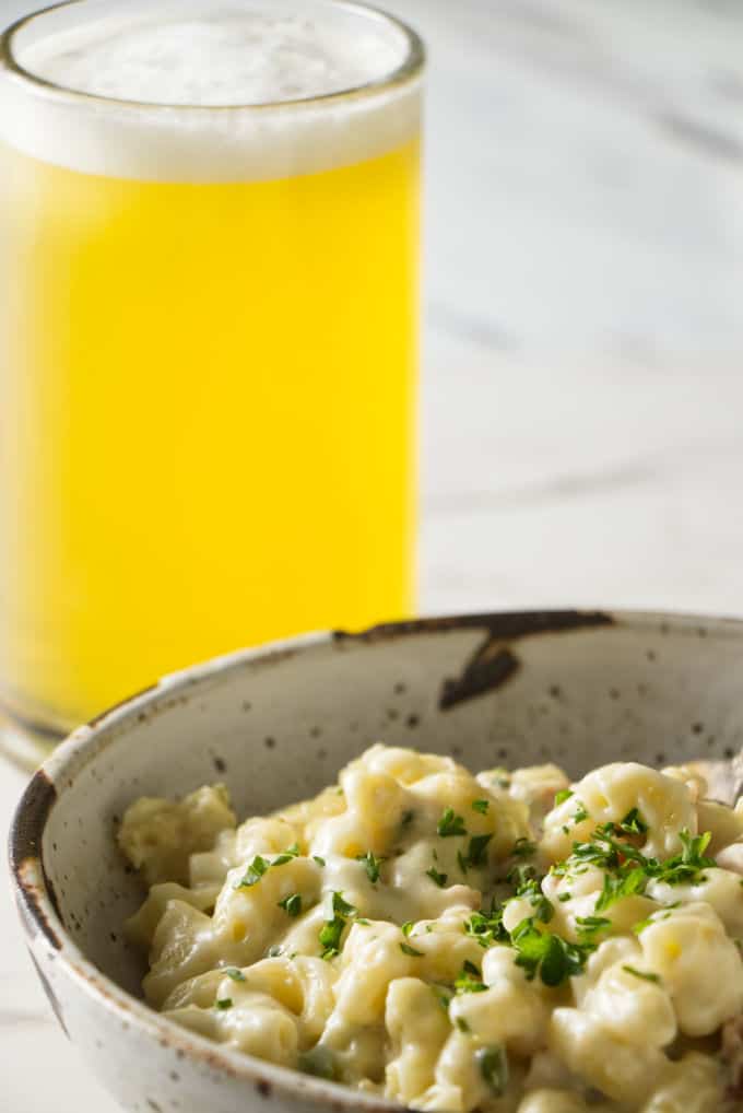 macaroni and cheese in a stone bowl with a spoon and topped with a green garnish a beer in the background