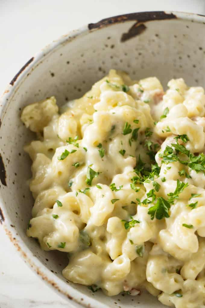 Macaroni and cheese with chunks of bacon and a creamy white cheese sauce in a stone bowl and with green garnish