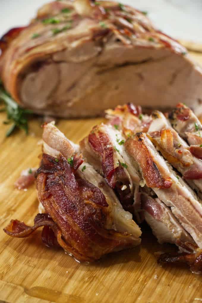 turkey breast wrapped in bacon and sliced sitting on a wooden cutting board with sage in the background