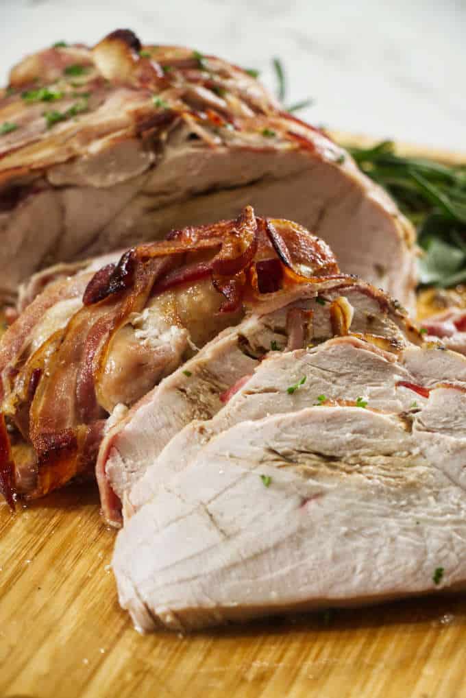 turkey breast wrapped in bacon and sliced sitting on a wooden cutting board with sage in the background