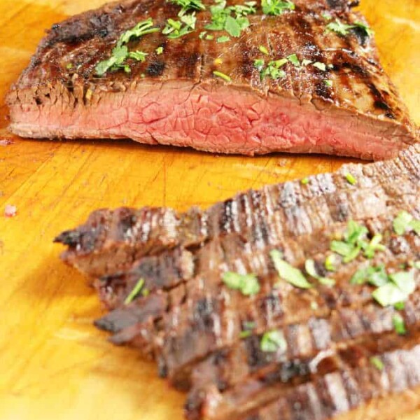 grilled flank steak on wood cutting board sliced into strips medium rare, veggies in background