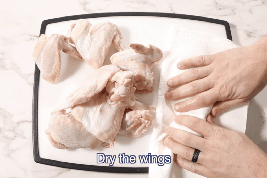 chicken wings on a white cutting board with black border being dried with a paper towel
