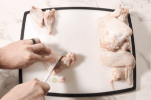 chicken wings on the cutting board and cutting with knife between wingette and drumette