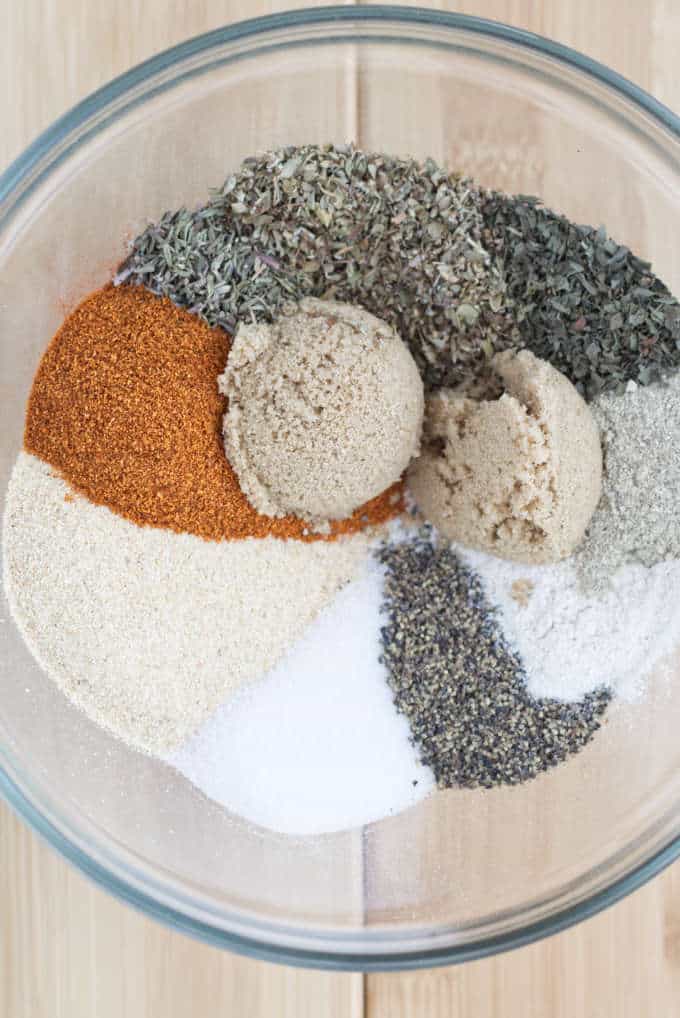 large glass mixing bowl full of spices but not combined, so they are all sitting separated into piles next to each other in a circular pattern sitting on a wooden table