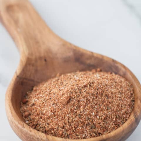 Large wooden spoon filled with brownish red cajun spice seasoning sitting on a marble table