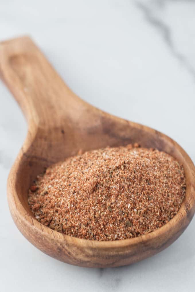 Large wooden spoon filled with brownish red cajun spice seasoning sitting on a marble table