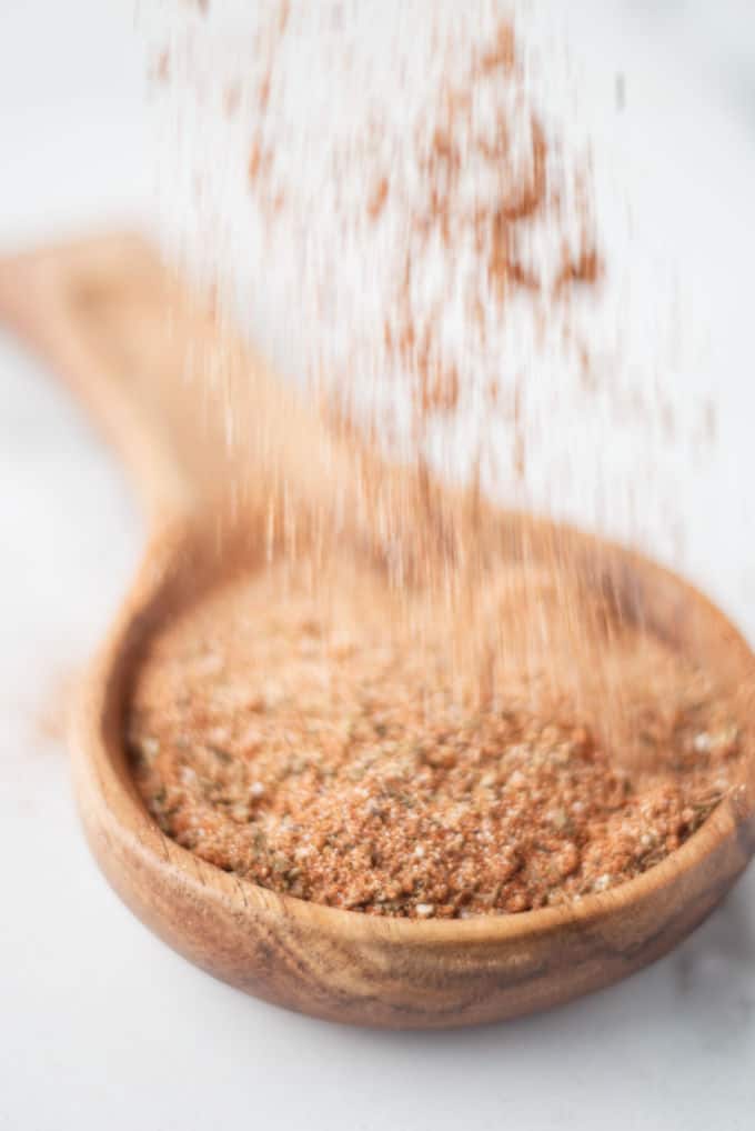 cajun spice sprinkling over large wooden spoon filled with brownish red cajun spice seasoning