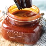 Kansas City-style BBQ sauce in a mason jar sitting on gray and white napkin with some loose seasoning on the table in front
