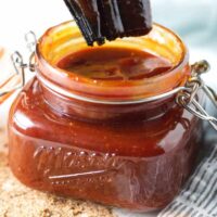 Kansas City-style BBQ sauce in a mason jar sitting on gray and white napkin with some loose seasoning on the table in front