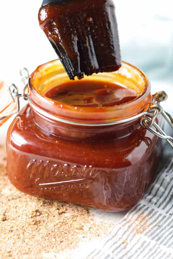 Kansas City-style BBQ sauce in a mason jar sitting on gray and white napkin with some loose seasoning on the table in front