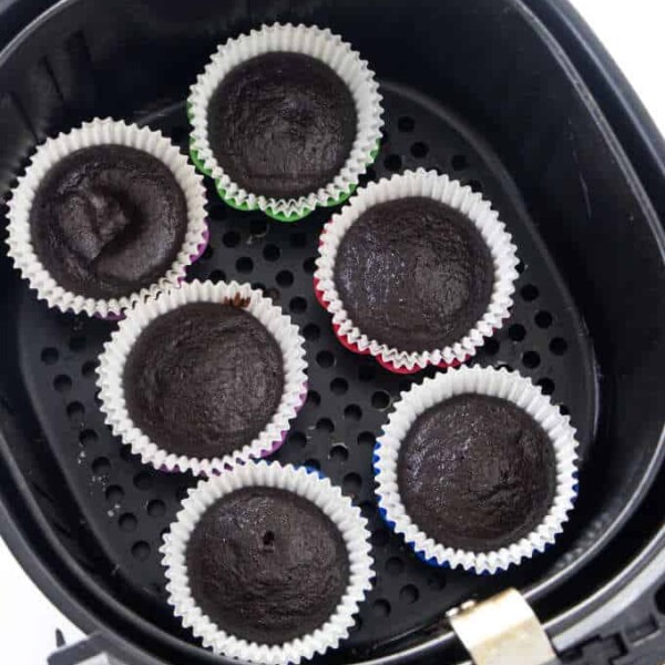 Six chocolate cupcakes in an air fryer basket.