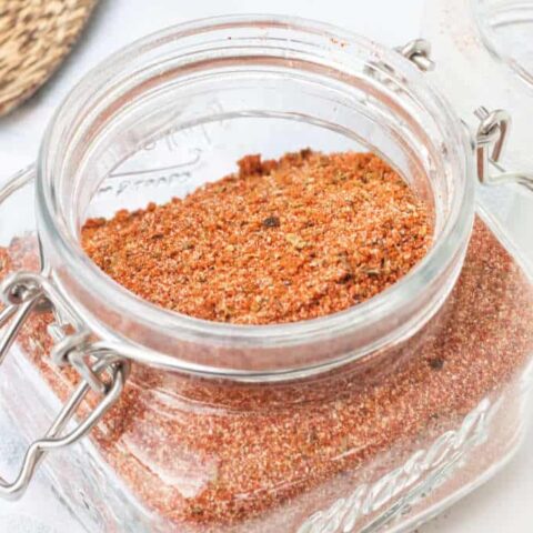 barbecue spice blend in an airtight mason jar with lid open wooden spoon in background on blue and white towel