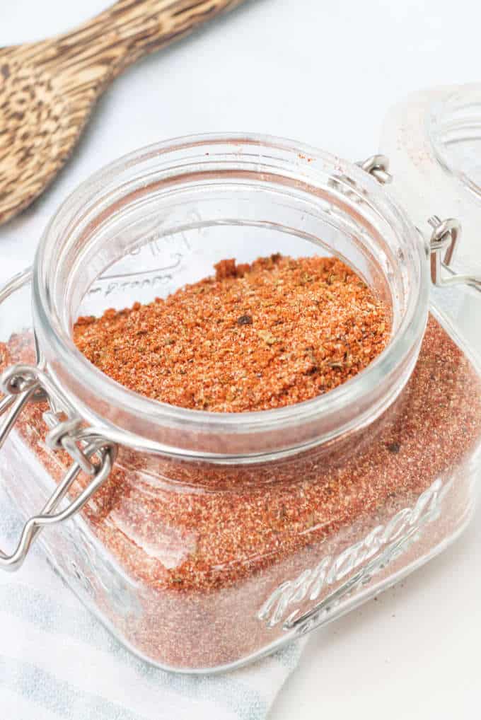 barbecue spice blend in an airtight mason jar with lid open wooden spoon in background on blue and white towel