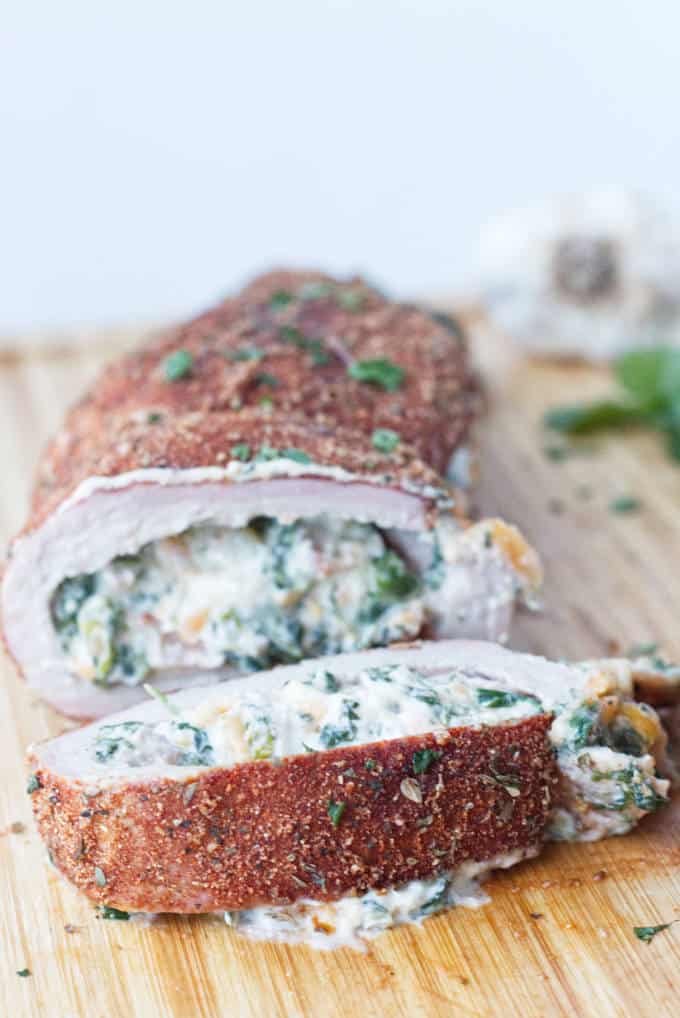 sliced stuffed pork tenderloin with cajun rub and twine holding it together, cheese stuffing, cilantro and garlic cloves sitting on wood
