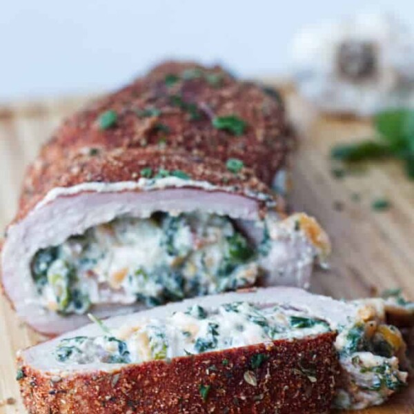 sliced stuffed pork tenderloin with cajun rub and twine holding it together, cheese stuffing, cilantro and garlic cloves sitting on wood