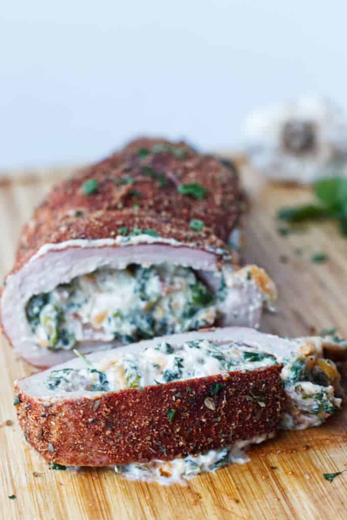 sliced stuffed pork tenderloin with cajun rub and twine holding it together, cheese stuffing, cilantro and garlic cloves sitting on wood