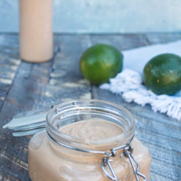 chipotle lime crema in a mason jar sitting on a wood plank surface with two whole limes in the background