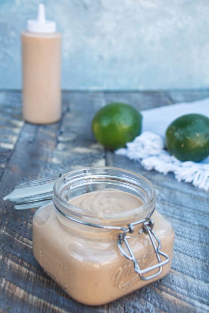 chipotle lime crema in a mason jar sitting on a wood plank surface with two whole limes in the background