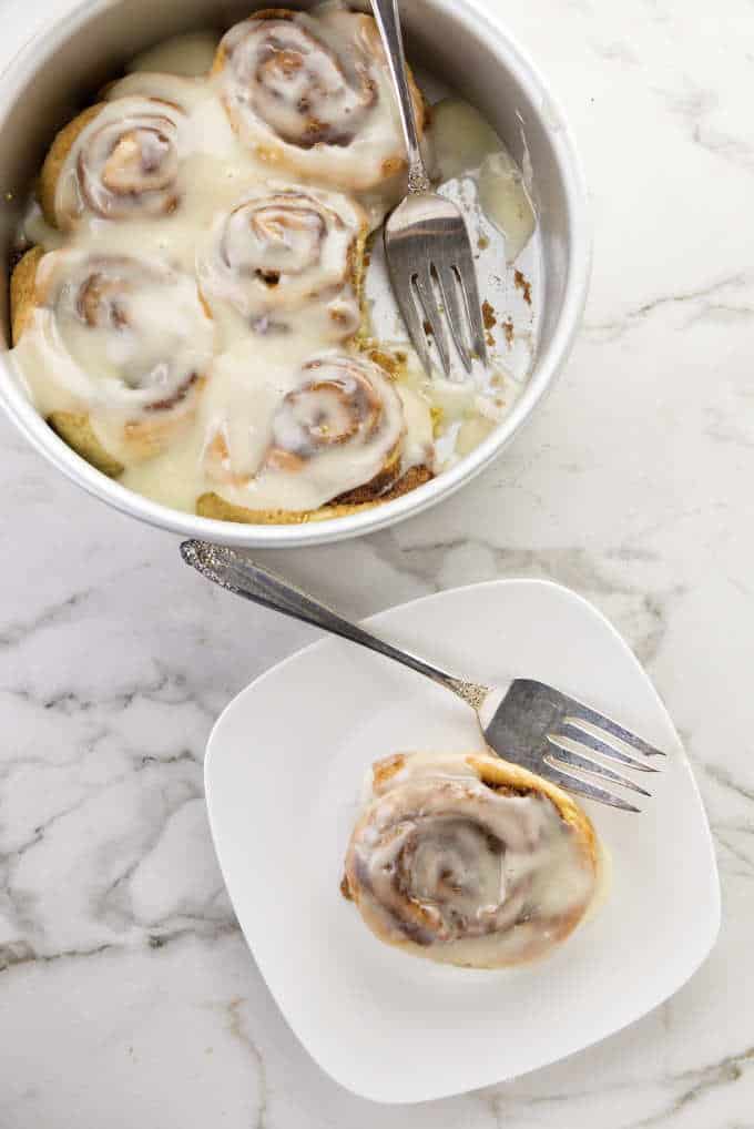 Five cinnamon rolls in a cake pan and one on a plate.