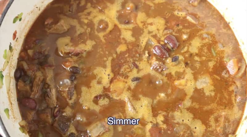 dutch oven filled with smoked brisket chili being simmered on low-medium heat burner