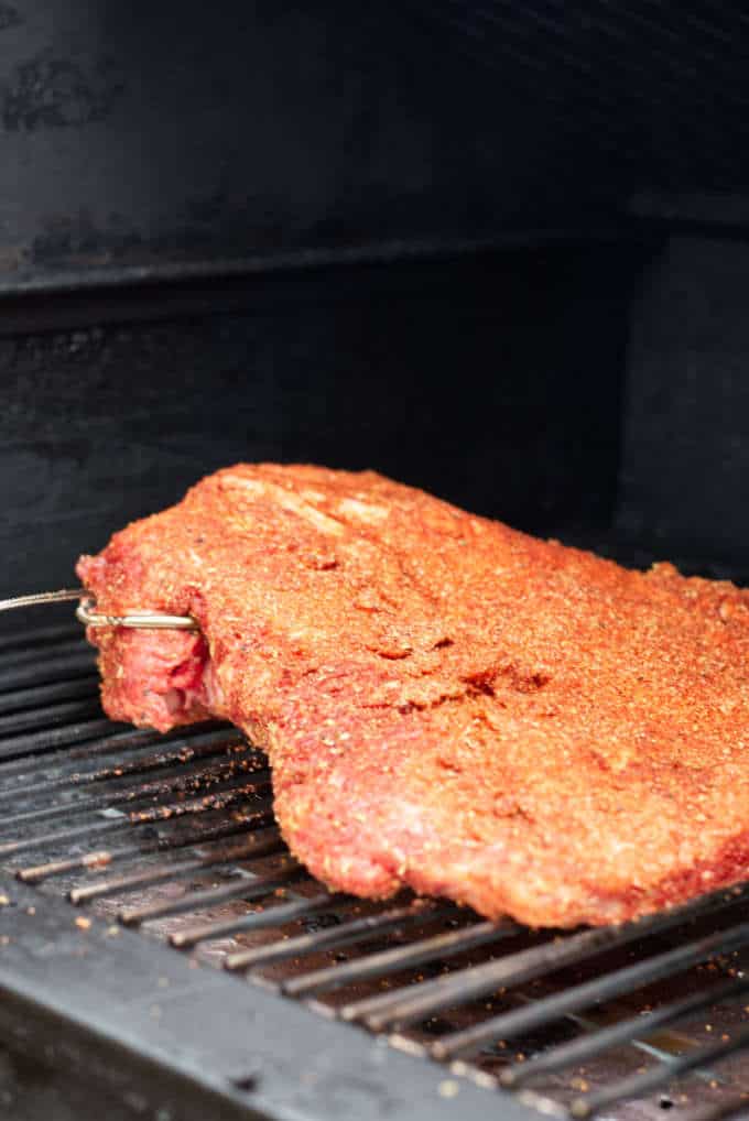 Brisket covered in dry rub sitting on the grill with temperature probe
