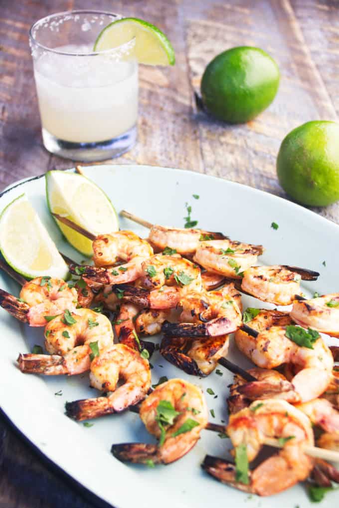 grilled tequila lime shrimp on a skewer with lime wedges and margarita and whole limes
