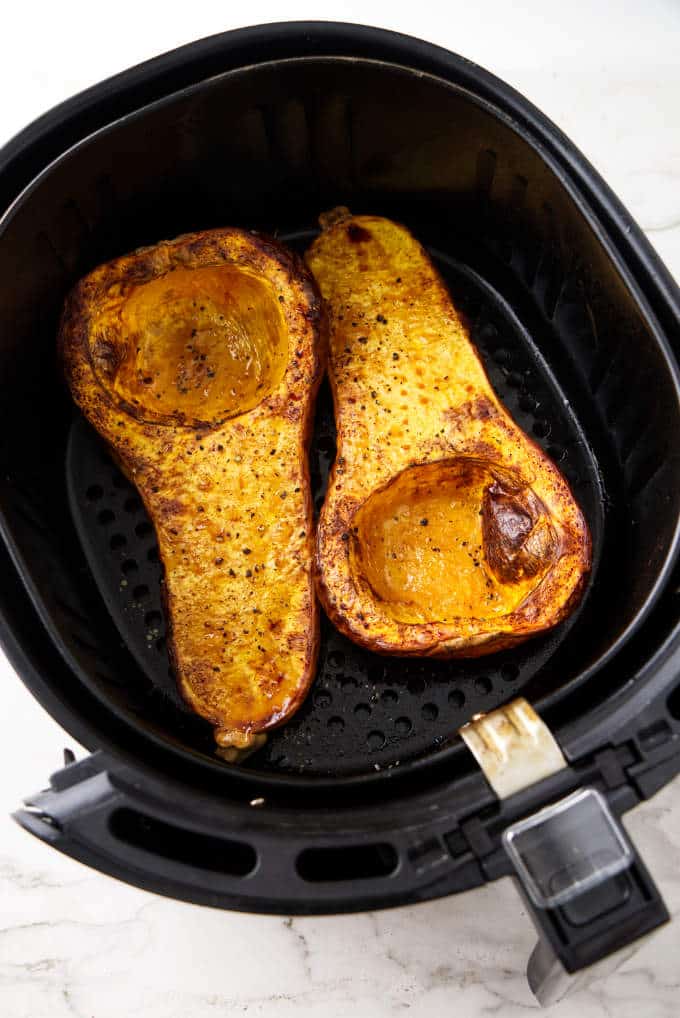Two halves of a butternut squash in an air fryer basket.