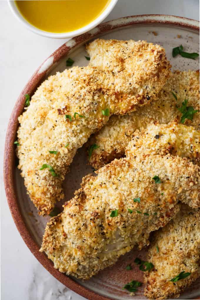 Several chicken tenders on a plate with dipping sauce.