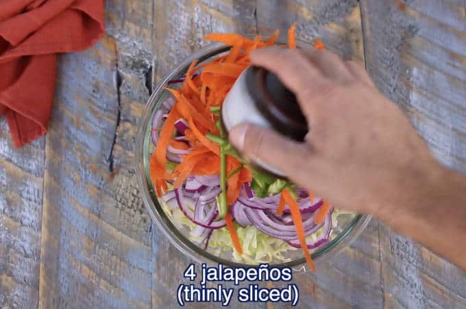 chopped vegetable ingredients for jalapeño lime cilantro slaw in a glass bowl on wood table