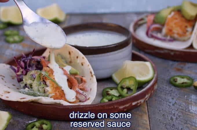 creamy sauce being drizzled over tilapia fish taco