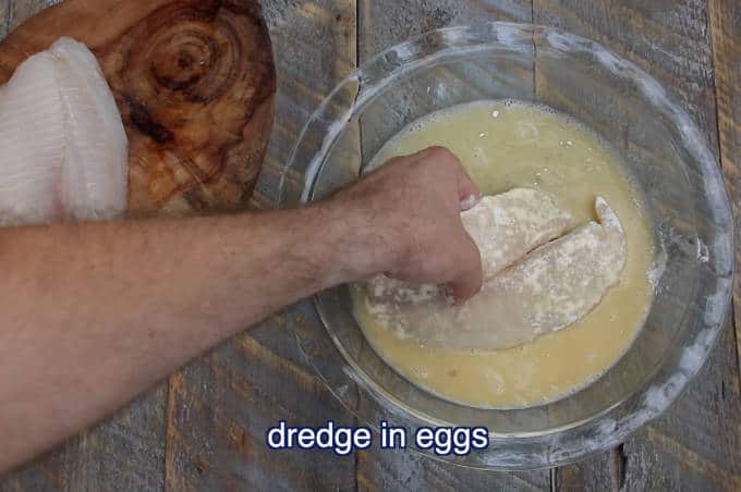 flour coated tilapia filet being dredged in beaten egg