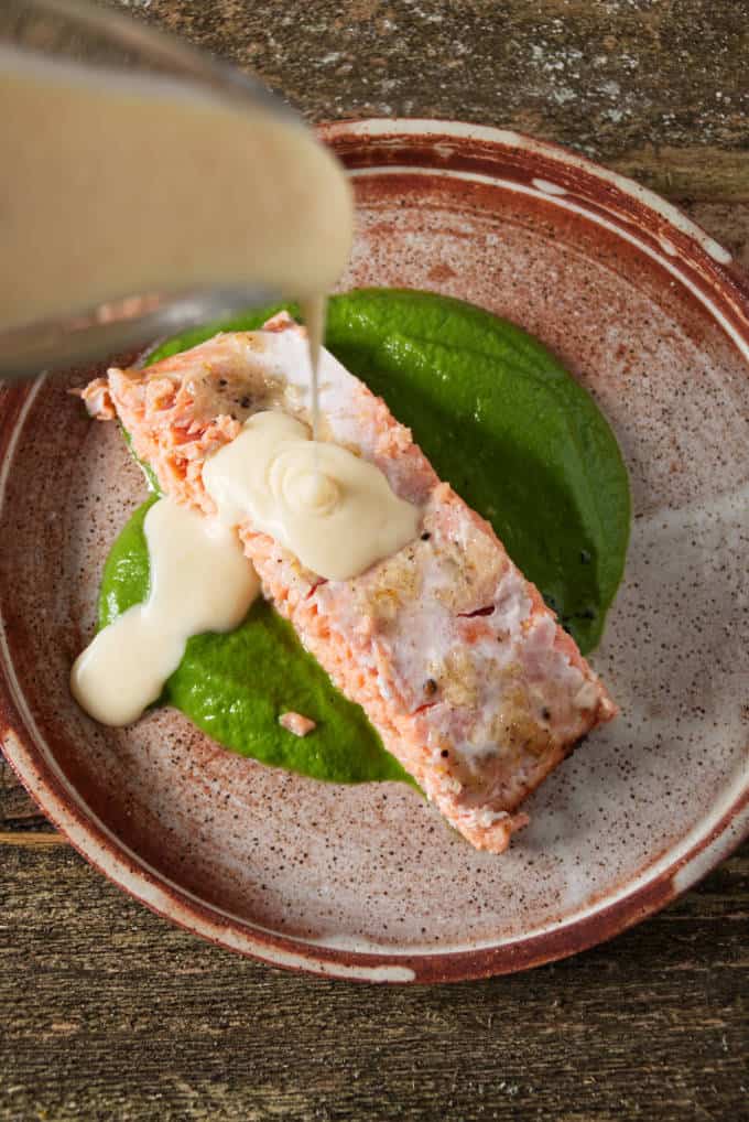 orange lemon butter sauce in gravy boat being drizzled over a salmon fillet