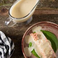 orange lemon butter sauce drizzled on top of a grilled salmon fillet with gravy boat of sauce